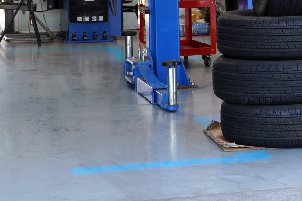 Automotive service shop floor with a blue vehicle lift base, stacked car tires, metal equipment, and blue safety markings