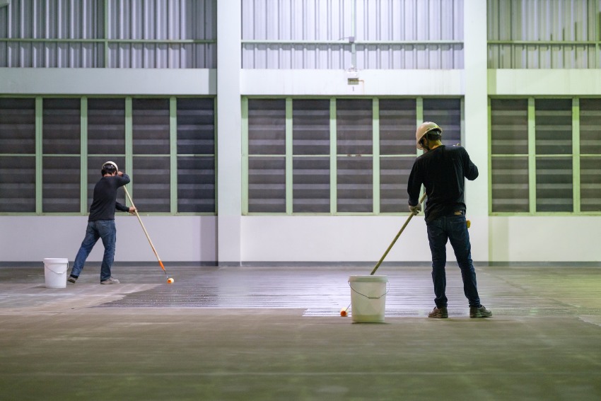 Workers applying protective floor coating in a large warehouse to improve surface performance